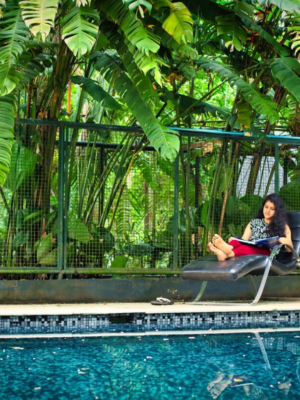 A tranquil pool relaxation area at Softouch Ayurveda Village in Kerala, showcasing comfortable lounge chairs, umbrellas, and a refreshing swimming pool surrounded by beautiful landscaping, creating an ideal space for relaxation and rejuvenation.